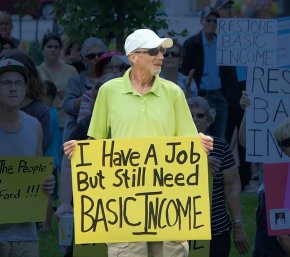 Man holding sign that says: I have a job but still need Basic Income