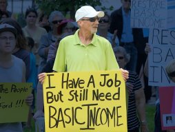 Man holding up sign that reads: I have a job but still Basic Income