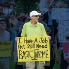 Man holding up sign that reads: I have a job but still Basic Income